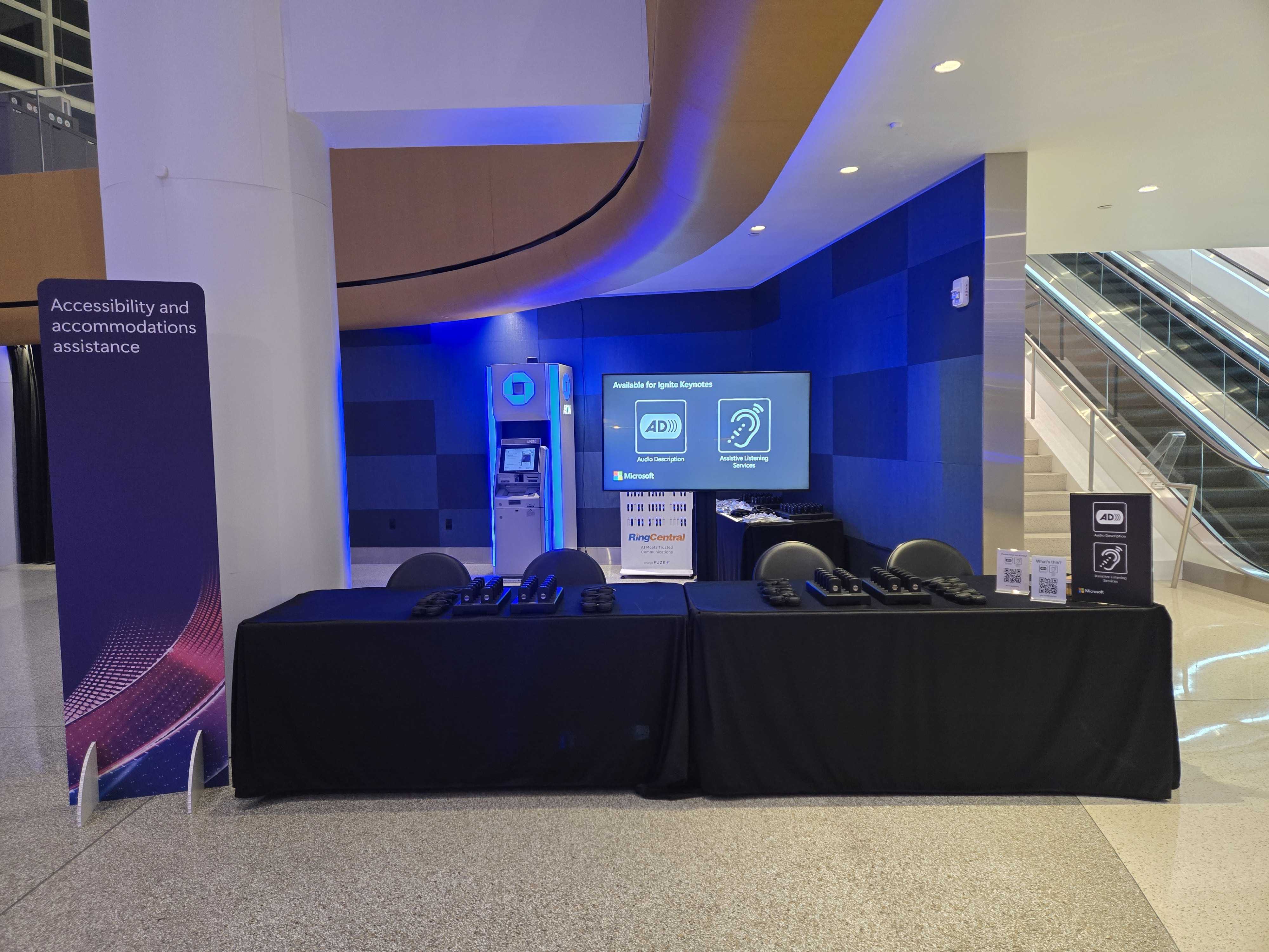 Accessibility assistance station at a conference featuring wireless listening devices, audio description services, and assistive listening equipment.
