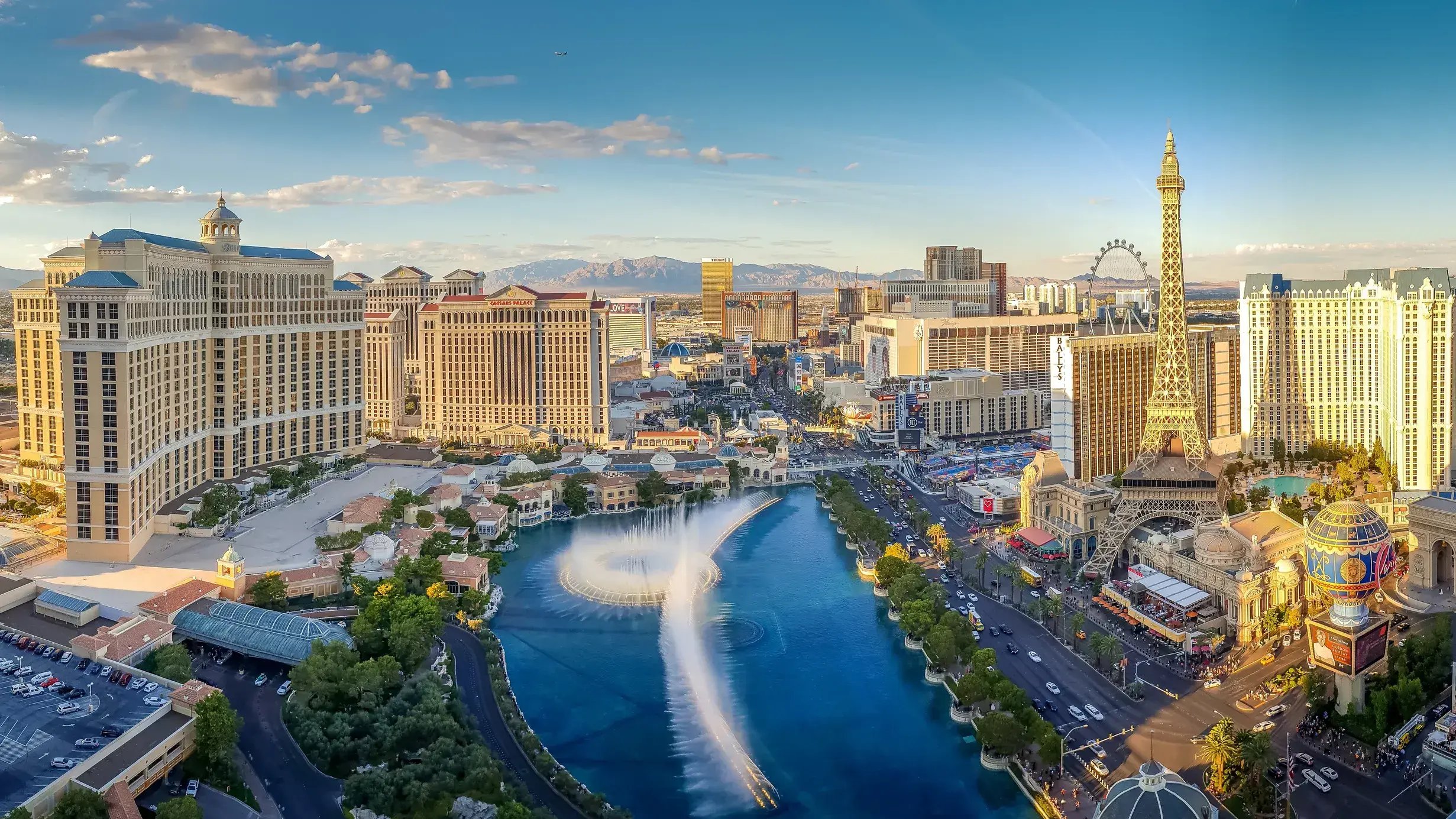 Aerial view of the Las Vegas Strip featuring the Bellagio fountains, Paris Las Vegas Eiffel Tower, surrounding hotels and distant mountains.