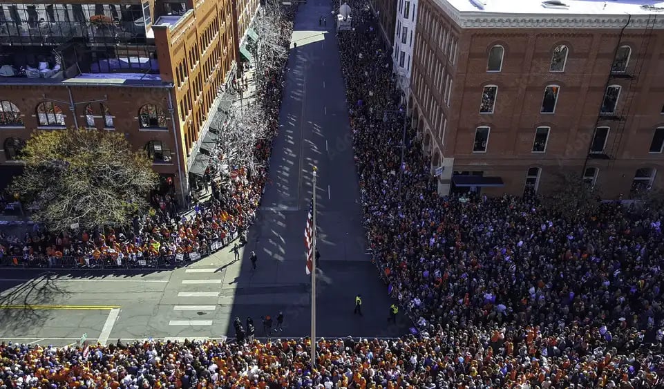 Thousands line a downtown street for a community parade with barricades and confetti.