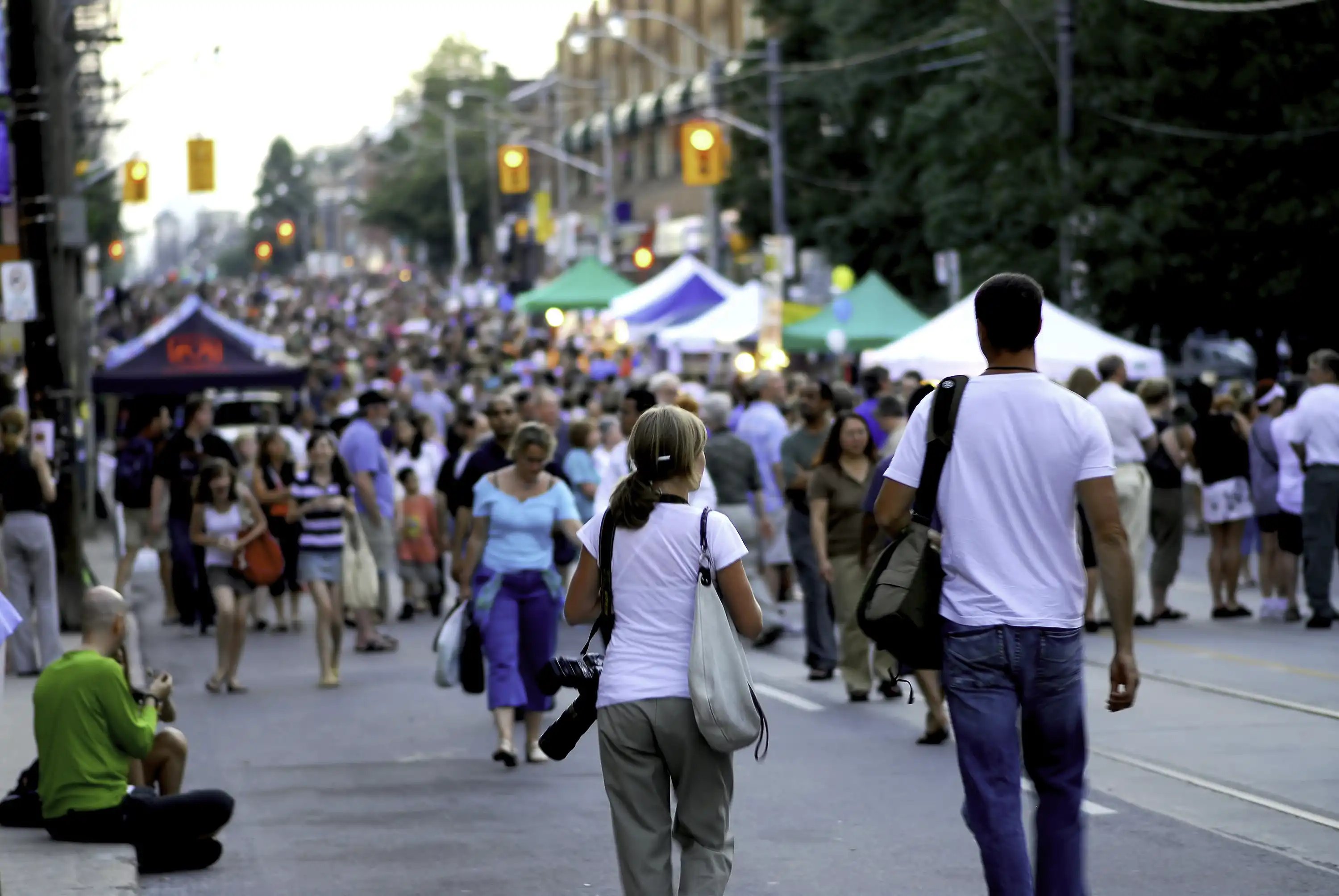 People fill a closed city street lined with booths and lights during a community event.