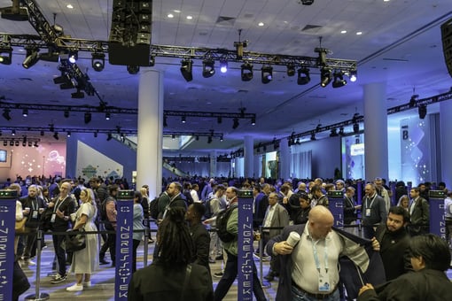 Attendees queue at check-in inside a spacious convention hall lit with truss lighting.