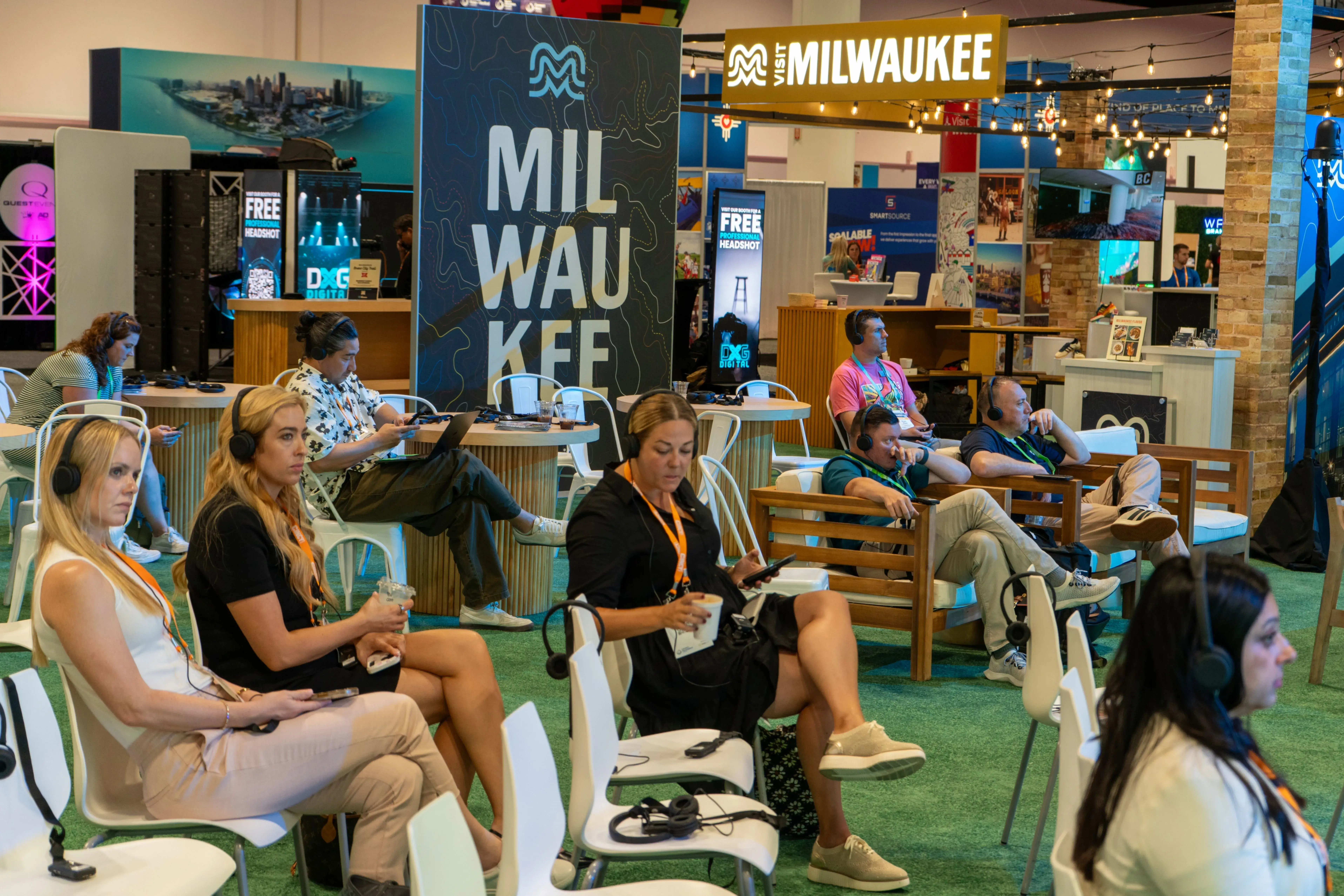 Conference attendees wearing wireless headsets listen to a silent session in a lounge seating area on a busy expo floor