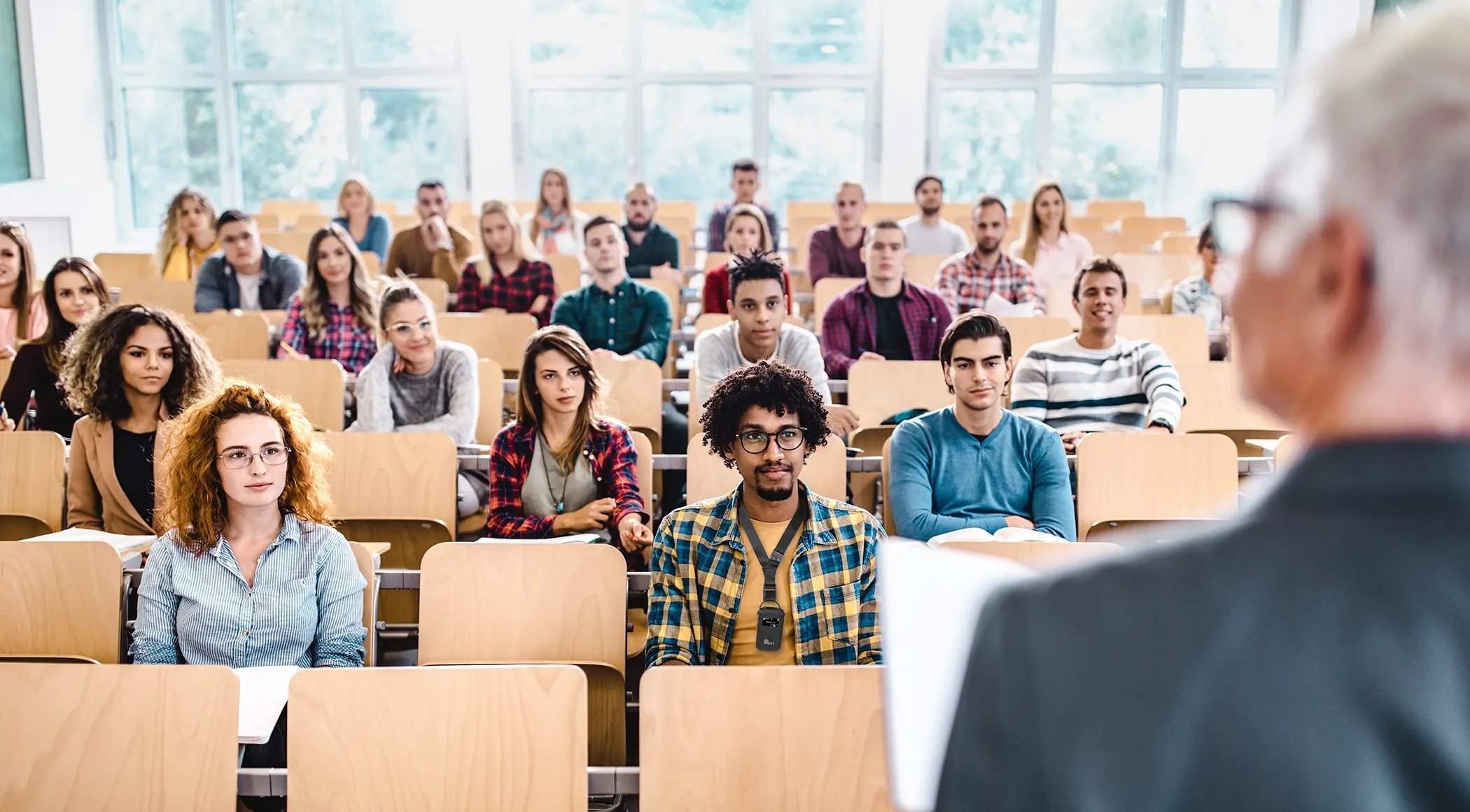 Students seated in a university lecture hall while one attendee wears an Auri receiver around his neck.