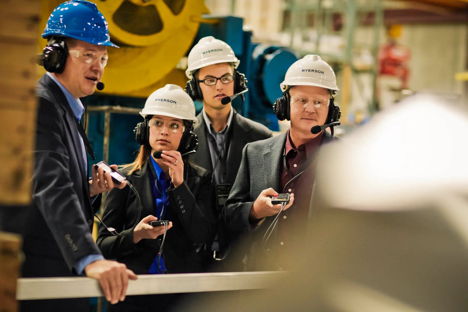 people-wearing-hardhats-and-headsets-infront-of-industiral-machinery